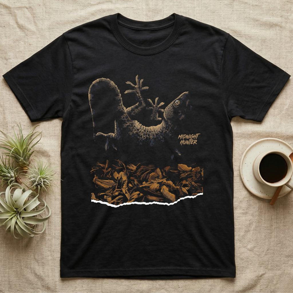 Illustration of a tokay gecko clinging upside-down above a torn wood-chip substrate, heavy stippled shading, text reading Midnight Hunter. — shown on a Black tee.