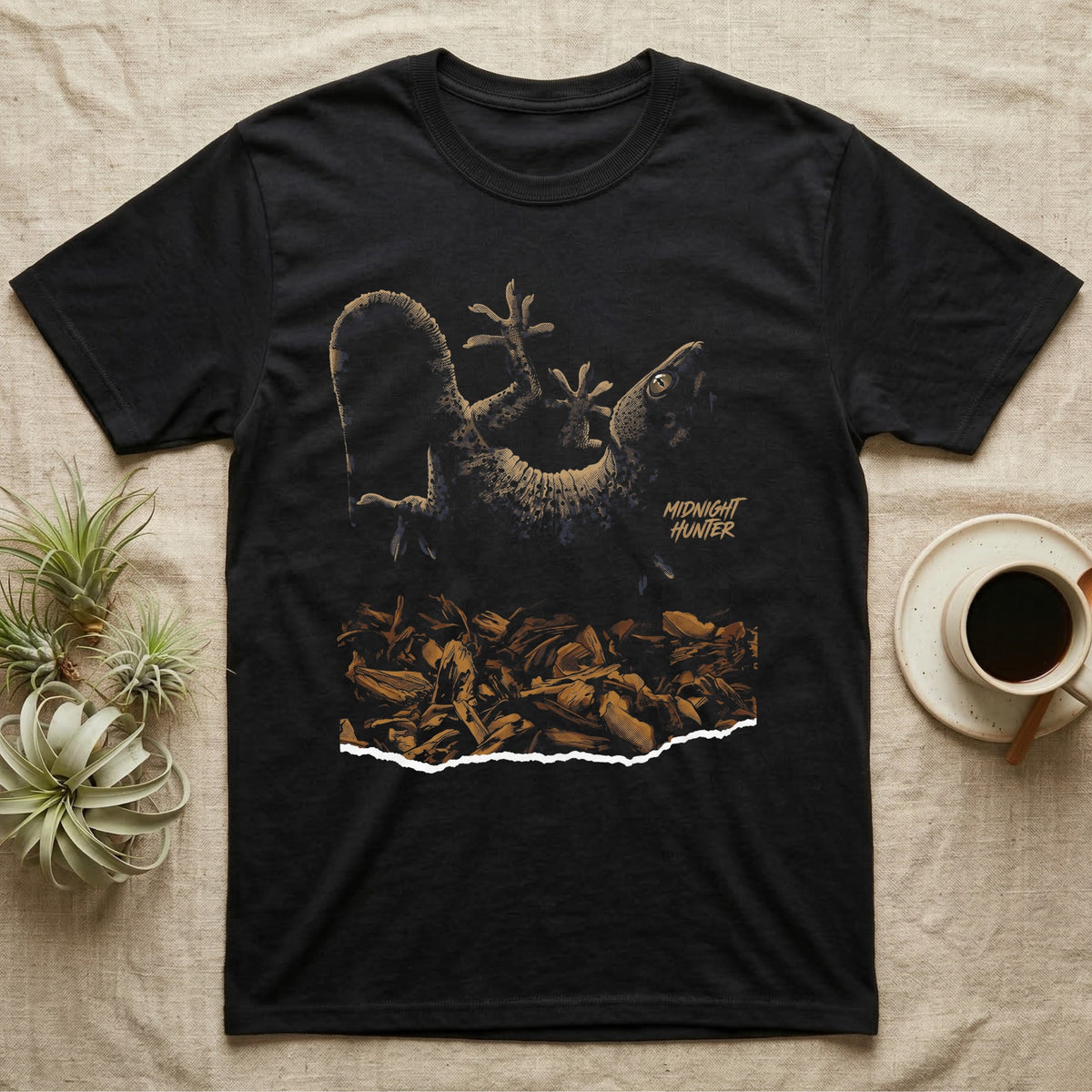 Illustration of a tokay gecko clinging upside-down above a torn wood-chip substrate, heavy stippled shading, text reading Midnight Hunter. — shown on a Black tee.