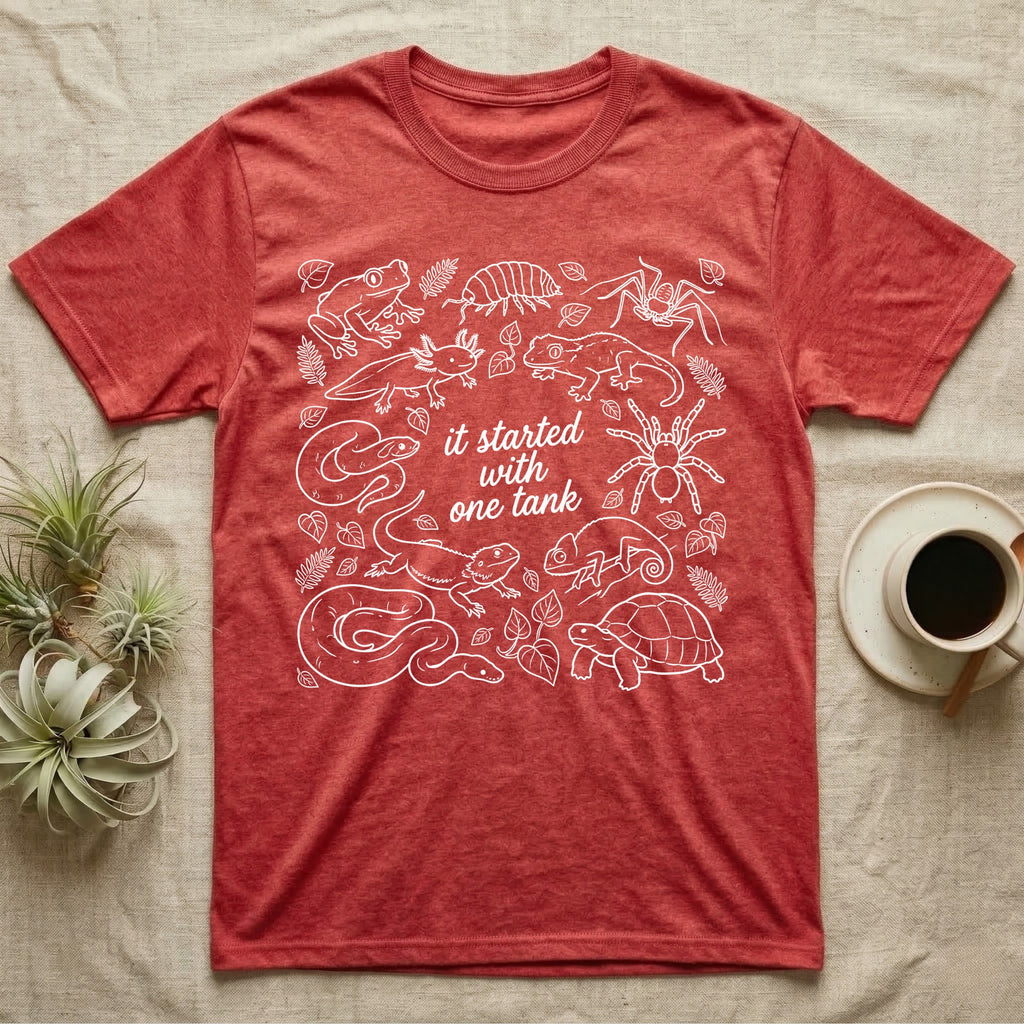 Terrarium Keeper One Tank T-Shirt in Heather Red — White outline illustration of eleven terrarium species — bearded dragon, crested gecko, ball python, axolotl, tortoise, tarantula, isopod, whip spider, chameleon, tree frog and hognose — with pothos and fern leaves, ringed around the script line it started with one tank.