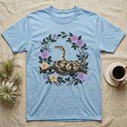 Ball Python Opinions Television T-Shirt in Light Blue — Oil-painted ball python coiled on a branch, enclosed by a dense oval bower of flowering bramble.