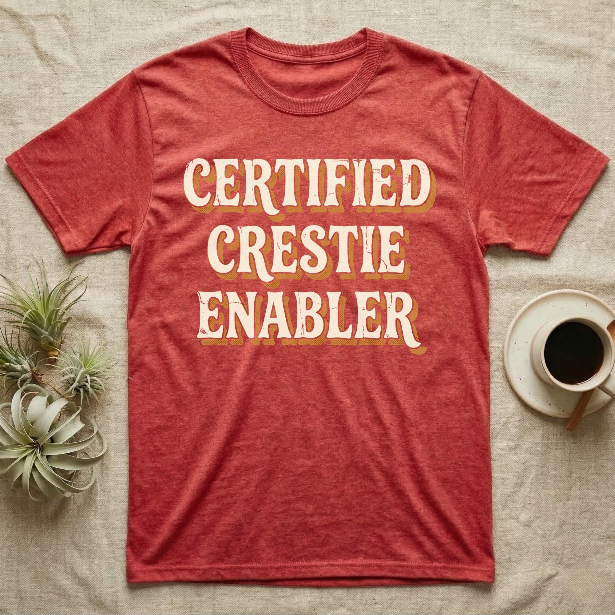Certified Crestie Enabler T-Shirt in Heather Red — Bold retro drop-shadow wordmark reading "Certified Crestie Enabler" in cream and ochre on a grey background.