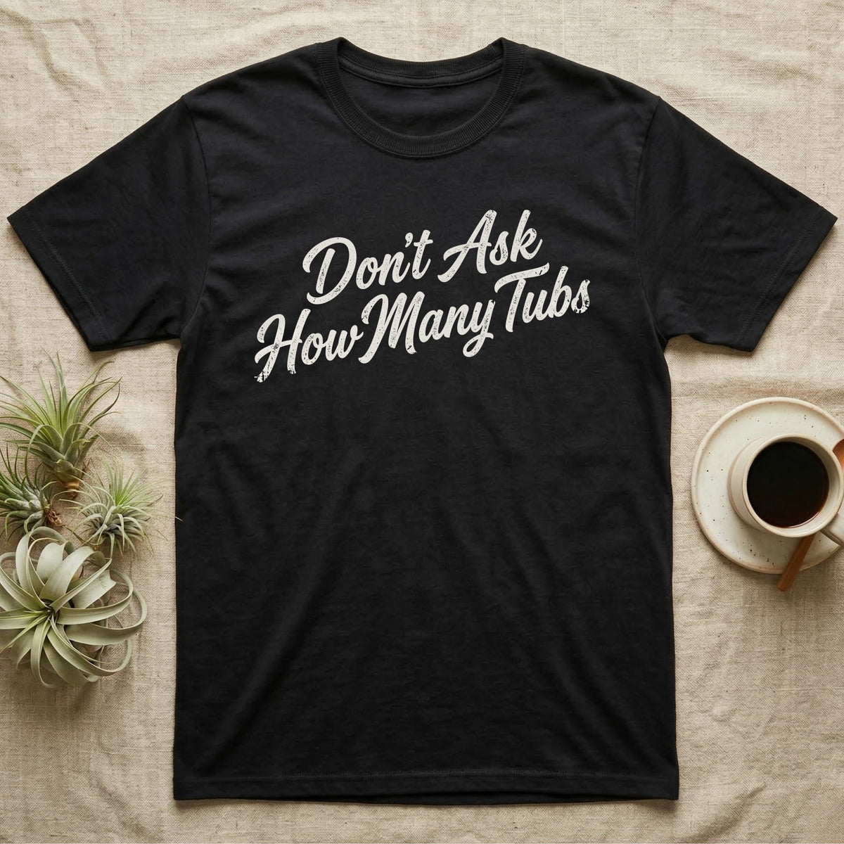 Snake Tubs T-Shirt in Black — Worn off-white 1970s retro brush script climbing a diagonal on charcoal, reading Don't Ask How Many Tubs