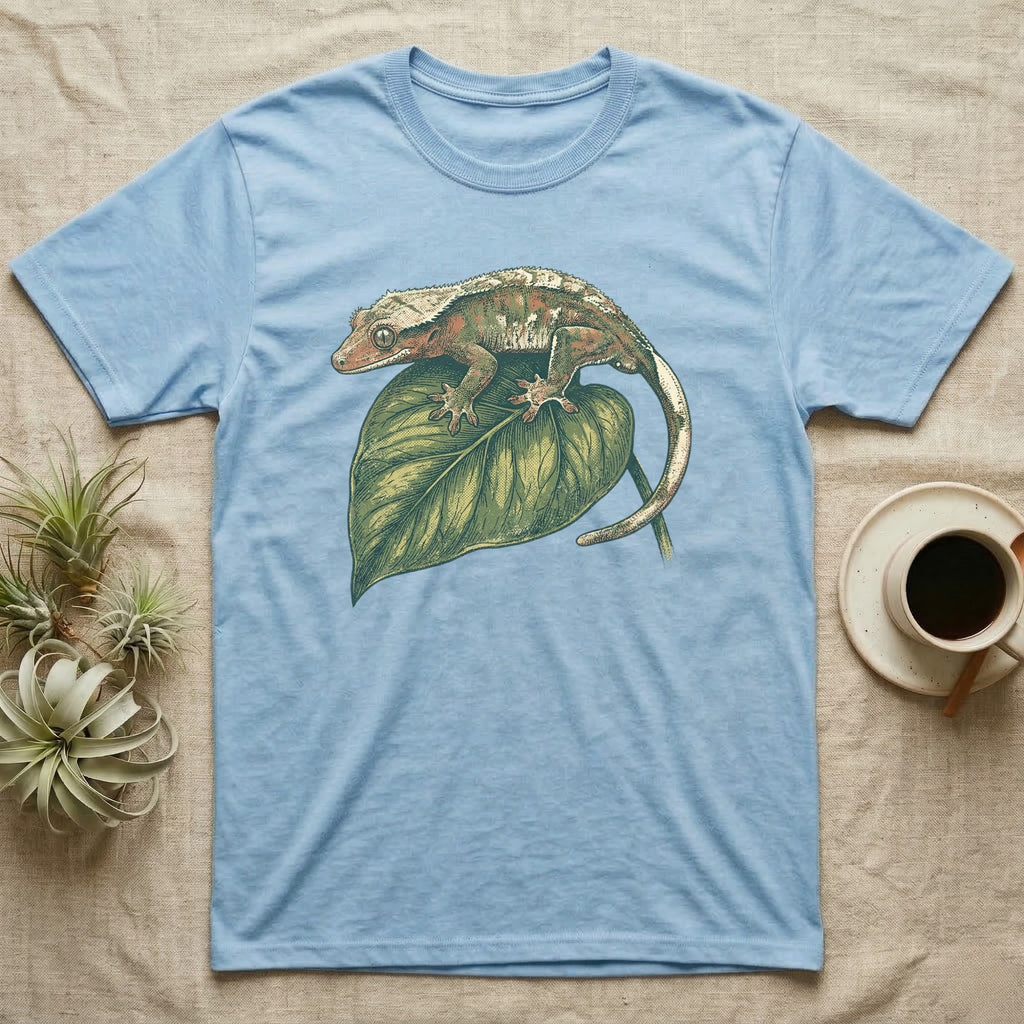 Light blue t-shirt with a crested gecko on a green leaf.