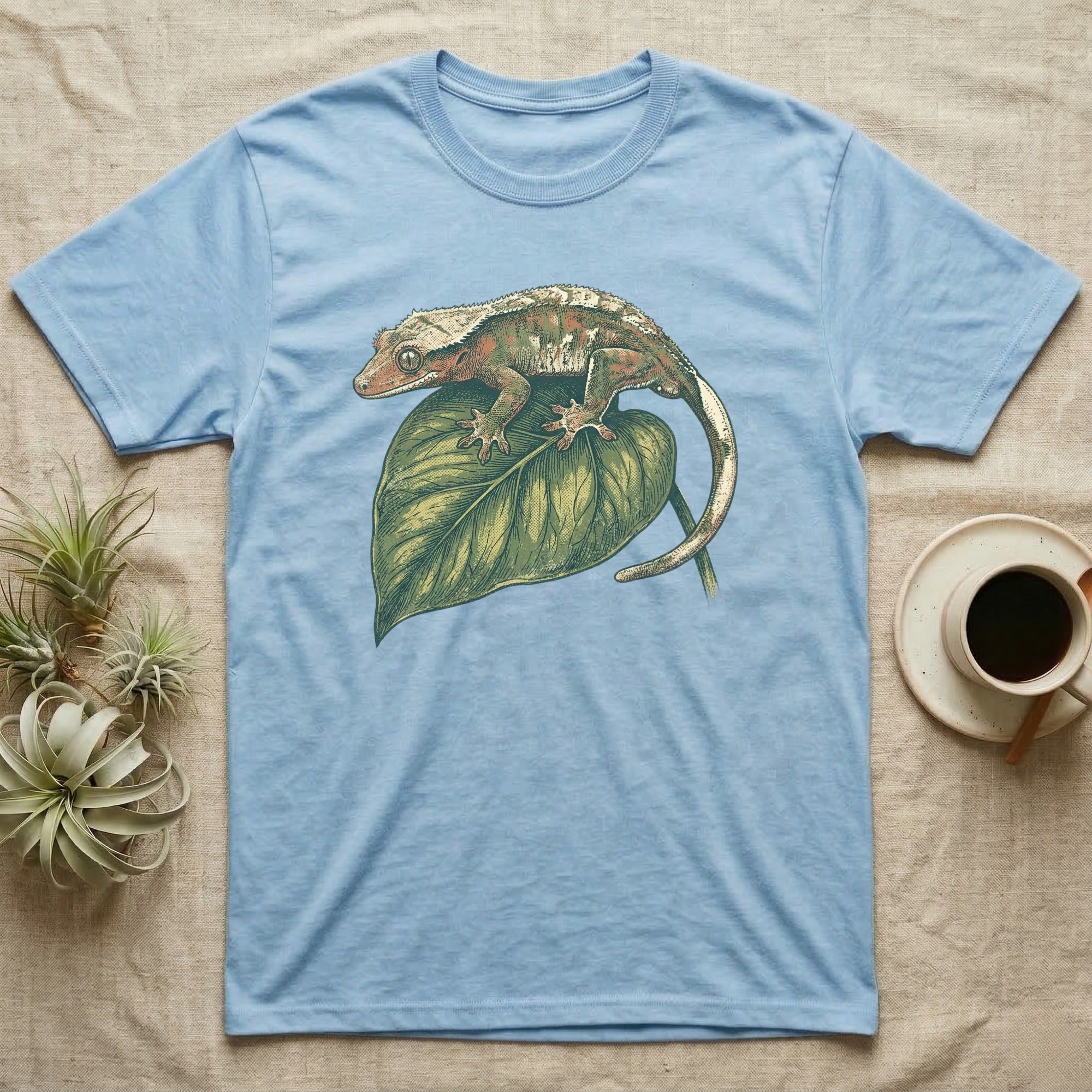 Light blue t-shirt with a crested gecko on a green leaf.