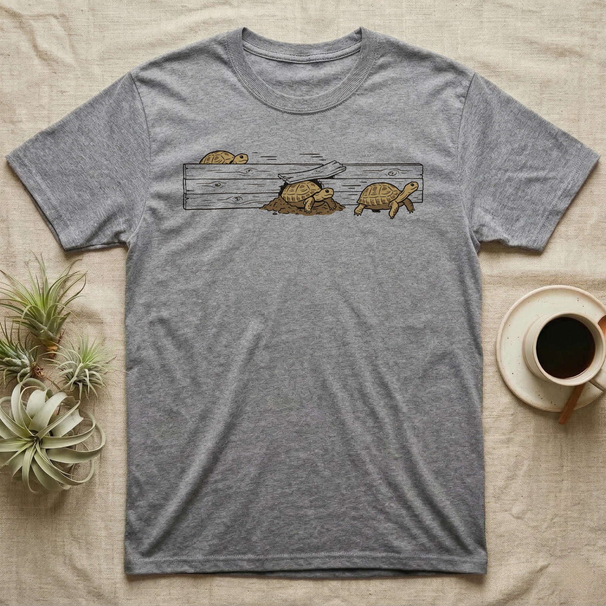 Russian Tortoise Escape Artist T-Shirt in Sport Grey — Clean ink run-cycle illustration of a Russian tortoise escaping its wooden tortoise-table enclosure in three phases.