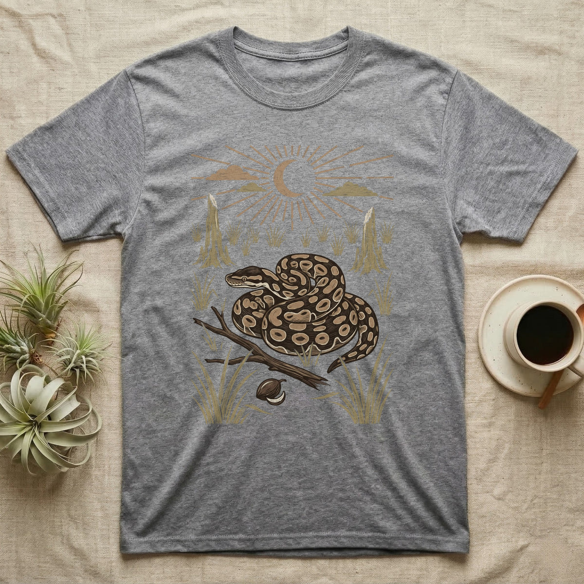 Ball Python Home Range T-Shirt in Sport Grey — Woodcut-style illustration of a ball python coiled on dry savanna ground with grass tufts and termite mounds behind, no on-shirt text.