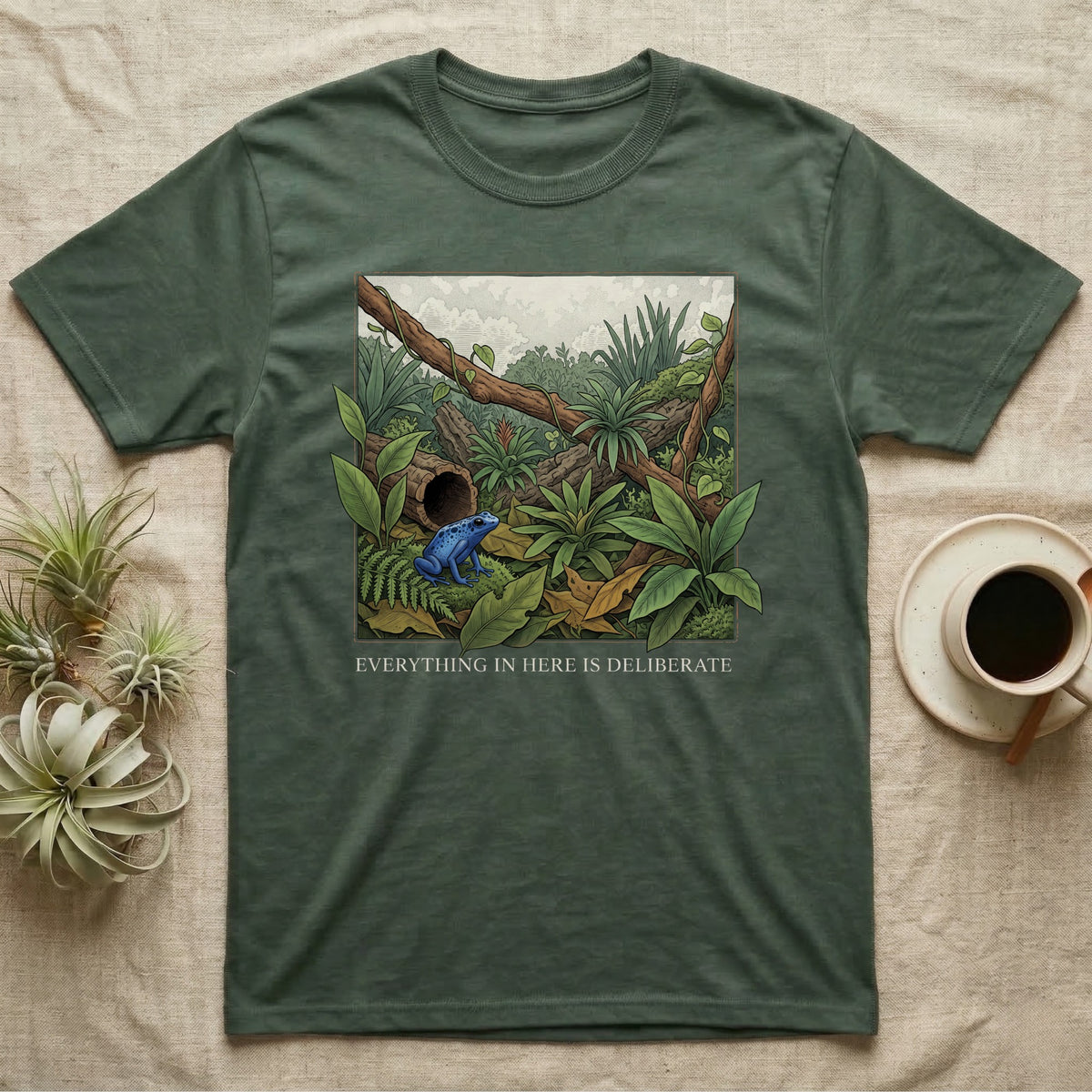 Dart Frog Bioactive Vivarium T-Shirt in Military Green — Illustrated panel of a cobalt dart frog in a layered planted vivarium, leaves crossing the inked border.