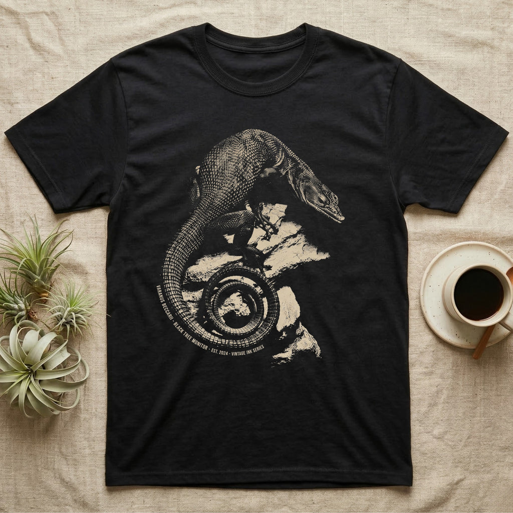 Vintage engraved illustration of a black tree monitor climbing rock with its tail coiled into a badge, arc text reading Varanus Beccarii, Black Tree Monitor, Est. 2024, Vintage Ink Series. — shown on a Black tee.