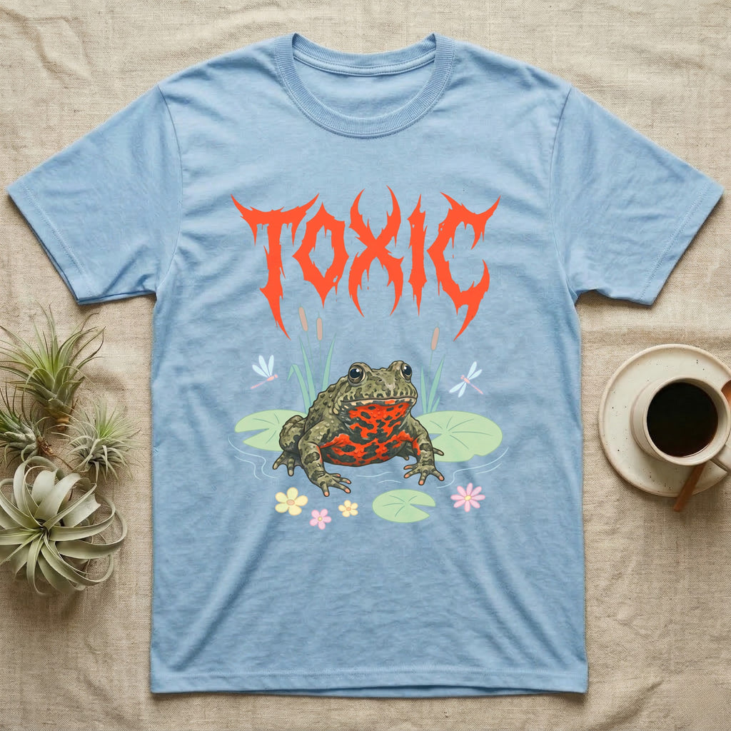 Oriental Fire-Bellied Toad Feral T-Shirt in Light Blue — Pastel fire-bellied toad with red-orange belly among lily pads and dragonflies, jagged metal wordmark "TOXIC" above.