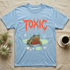 Oriental Fire-Bellied Toad Feral T-Shirt in Light Blue — Pastel fire-bellied toad with red-orange belly among lily pads and dragonflies, jagged metal wordmark "TOXIC" above.