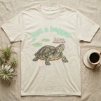 Red-Eared Slider Softie T-Shirt in Natural — Red-eared slider turtle stretching its neck to beg, under pastel bubble text "just a beggar" with hearts.