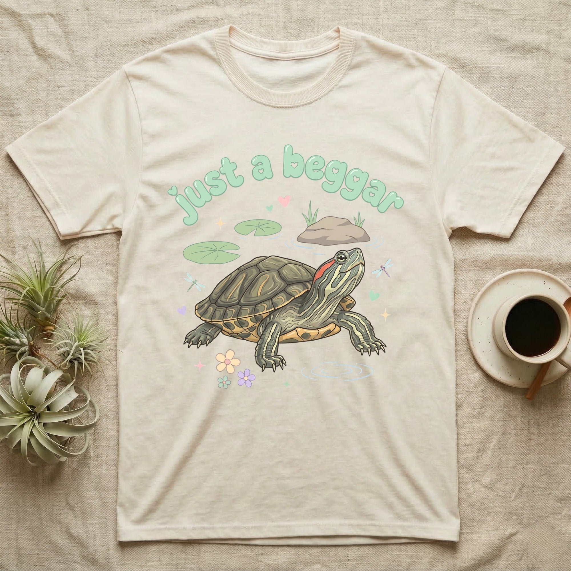 Red-Eared Slider Softie T-Shirt in Natural — Red-eared slider turtle stretching its neck to beg, under pastel bubble text "just a beggar" with hearts.