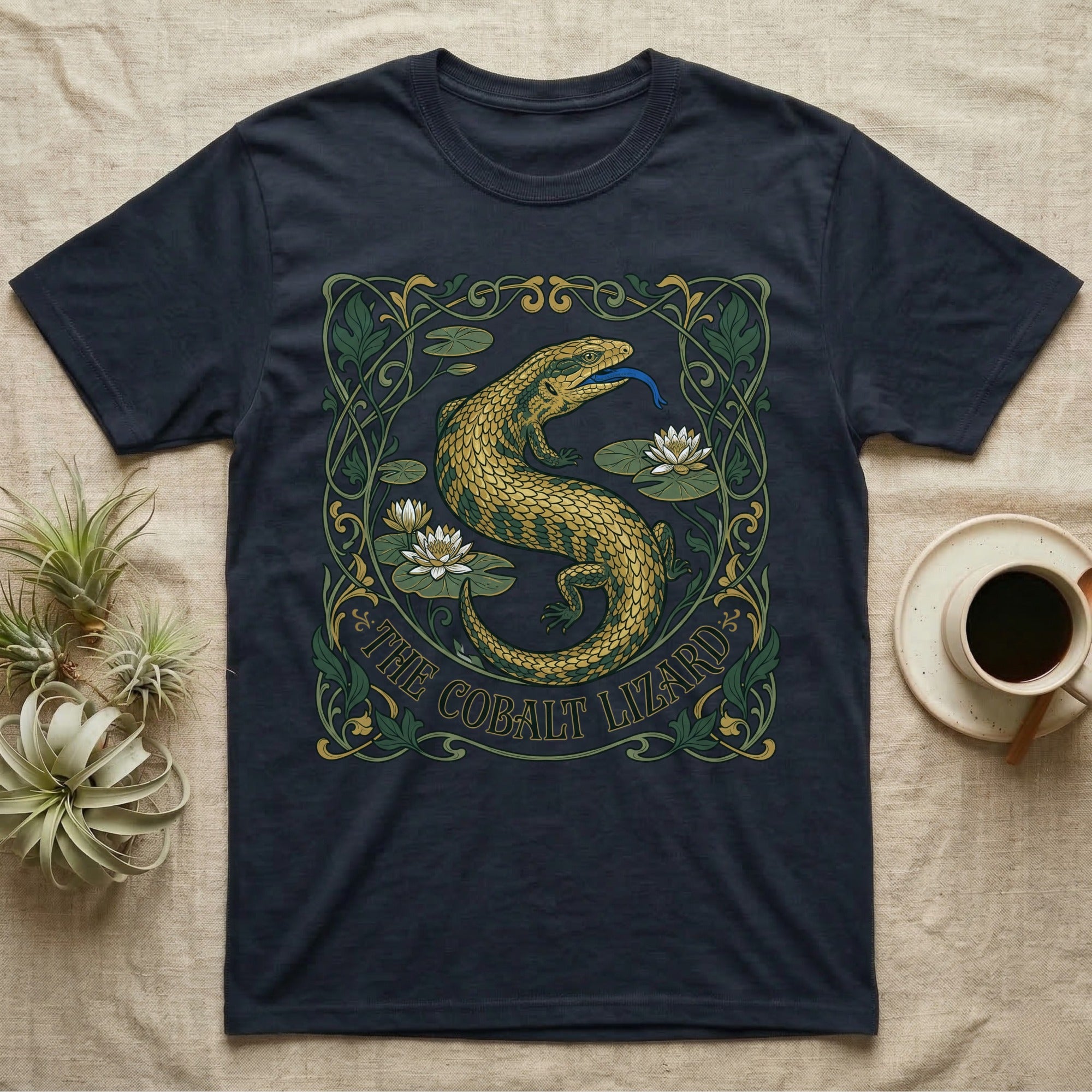 Dark t-shirt featuring a golden lizard in an art nouveau floral border with "The Cobalt Lizard" text.