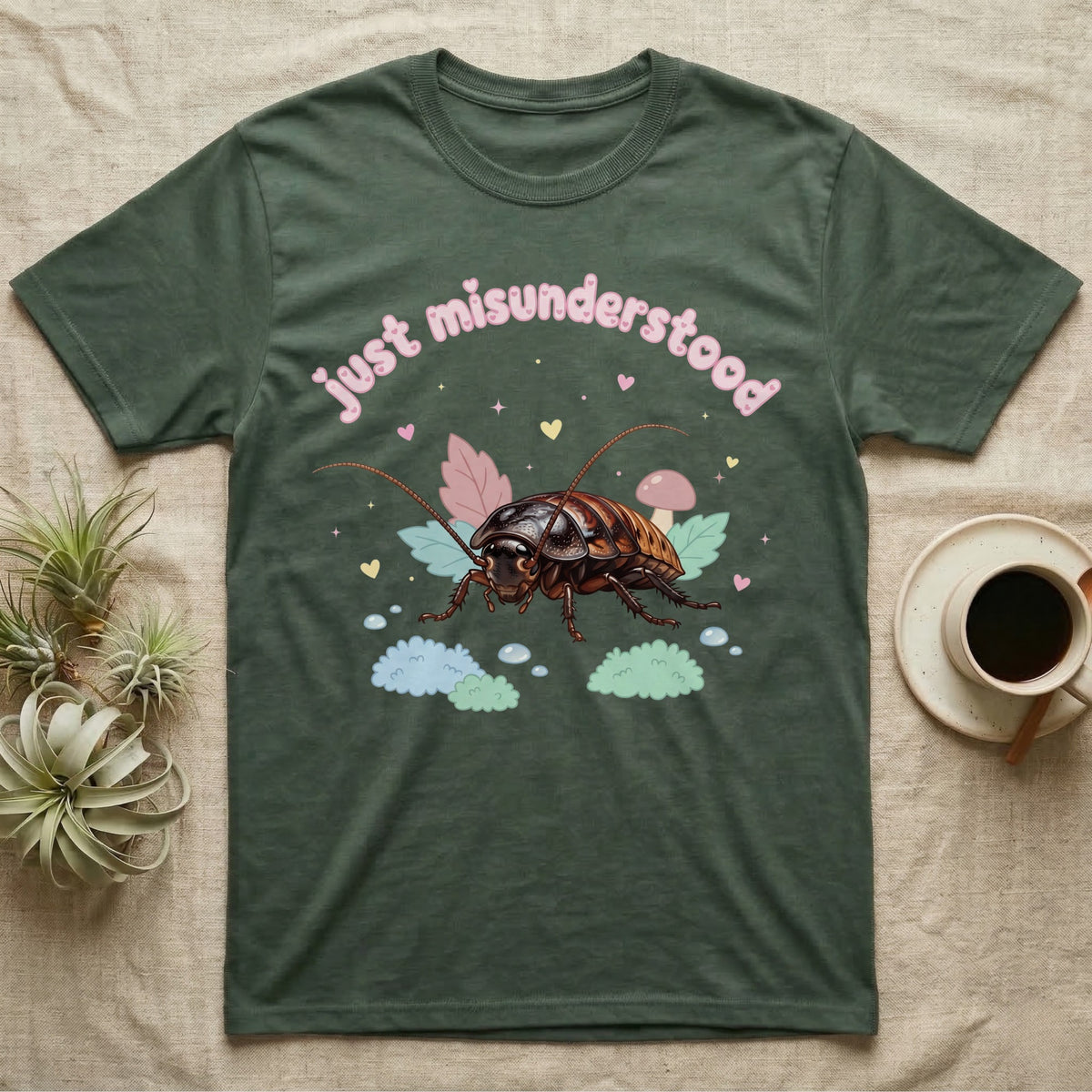 Madagascar Hissing Cockroach Baby T-Shirt in Military Green — Pastel Madagascar hissing cockroach among leaves, mushroom and moss, puffy pink wordmark "just misunderstood" above.