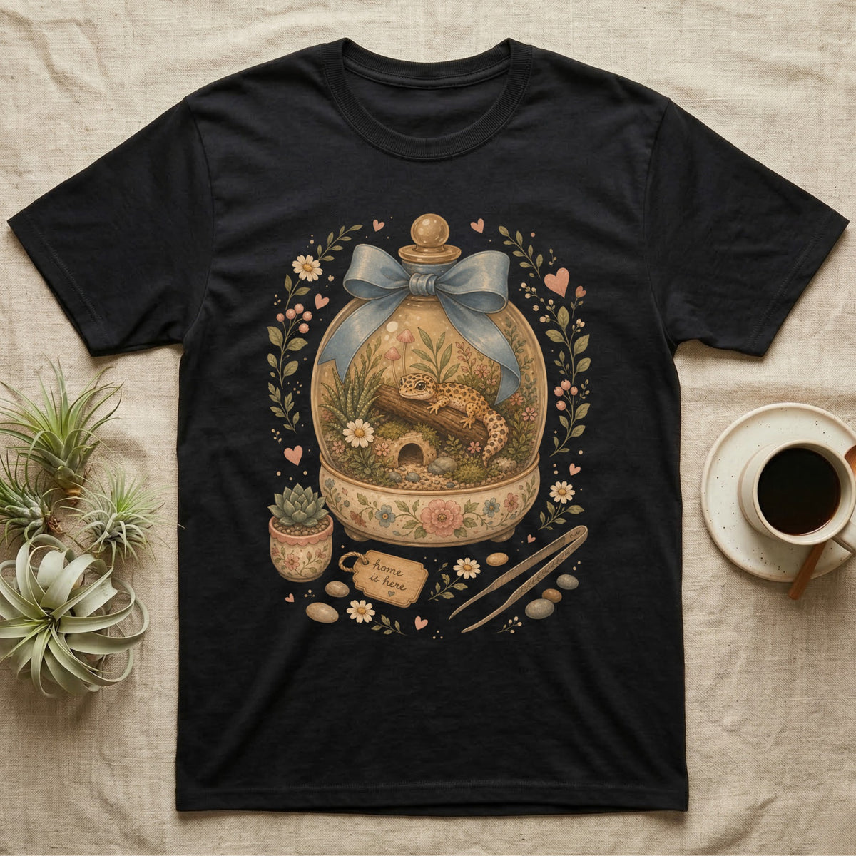 Black t-shirt with a graphic of a gecko in a terrarium with floral accents.