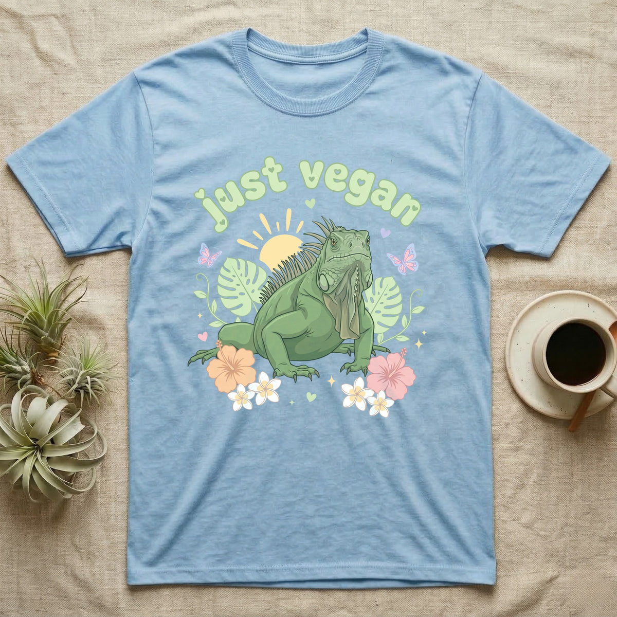 Green Iguana Baby T-Shirt in Light Blue — Green iguana with spiky crest and dewlap among pastel leaves and flowers under puffy green bubble text "just vegan".