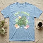 Green Iguana Baby T-Shirt in Light Blue — Green iguana with spiky crest and dewlap among pastel leaves and flowers under puffy green bubble text "just vegan".