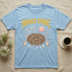 Ball Python Feral T-Shirt in Light Blue — Ball python coiled in a loaf in a pastel savanna scene under a spiky honey-gold metal wordmark reading HUNGER STRIKE.
