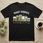 Reptile Terrarium Hobbies T-Shirt in Black — Watercolour row of reptile vivariums with a snake, dart frog, gecko, bearded dragon, tree frog and a cricket bin under MANY HOBBIES, each labelled carpentry to bug farming