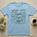 Reptile Expo T-Shirt in Light Blue — Green marker cursive reading Reptile Expo just looking, ringed by doodles of deli cups, tubs, a gecko and a tortoise