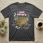 African Bullfrog Baby T-Shirt in Dark Heather — Pastel African bullfrog eyeing a tiny bug among reeds and flowers, puffy pink bubble wordmark "just hungry" above.