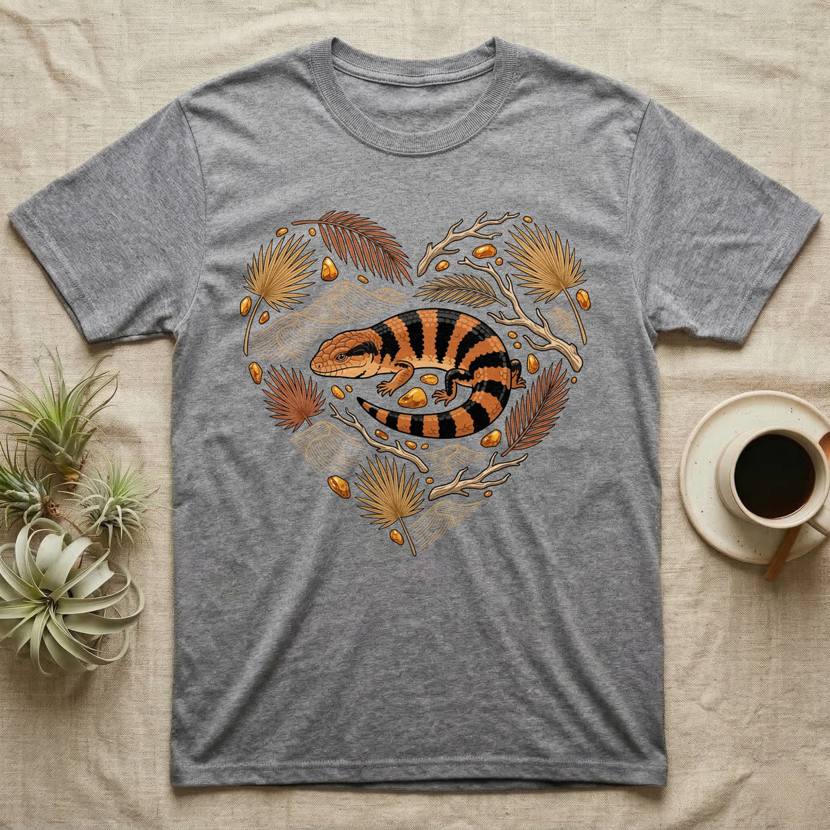 Gray t-shirt with a lizard and botanical elements in a heart shape.