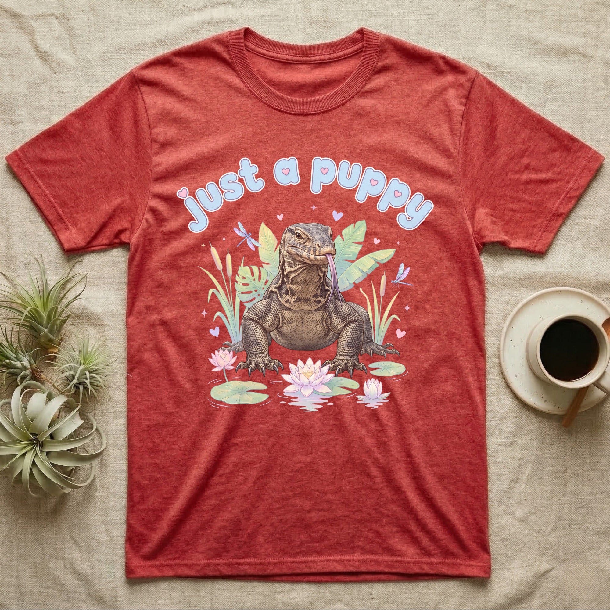 Asian Water Monitor Baby T-Shirt in Heather Red — Asian water monitor with tongue out among pastel reeds and lotus under puffy blue bubble text "just a puppy".