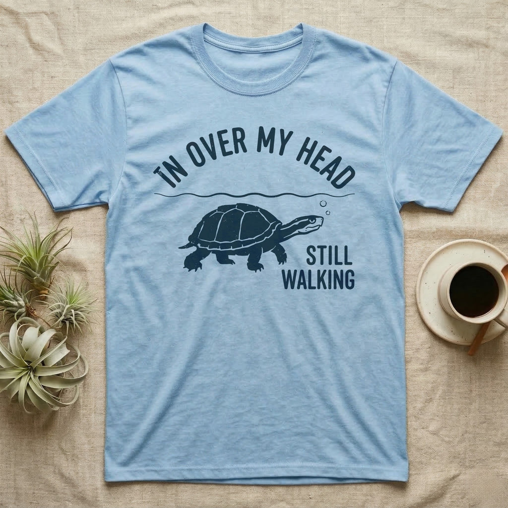 Musk Turtle Walking T-Shirt in Light Blue — Navy silhouette of a musk turtle walking under arched words In Over My Head, beside Still Walking