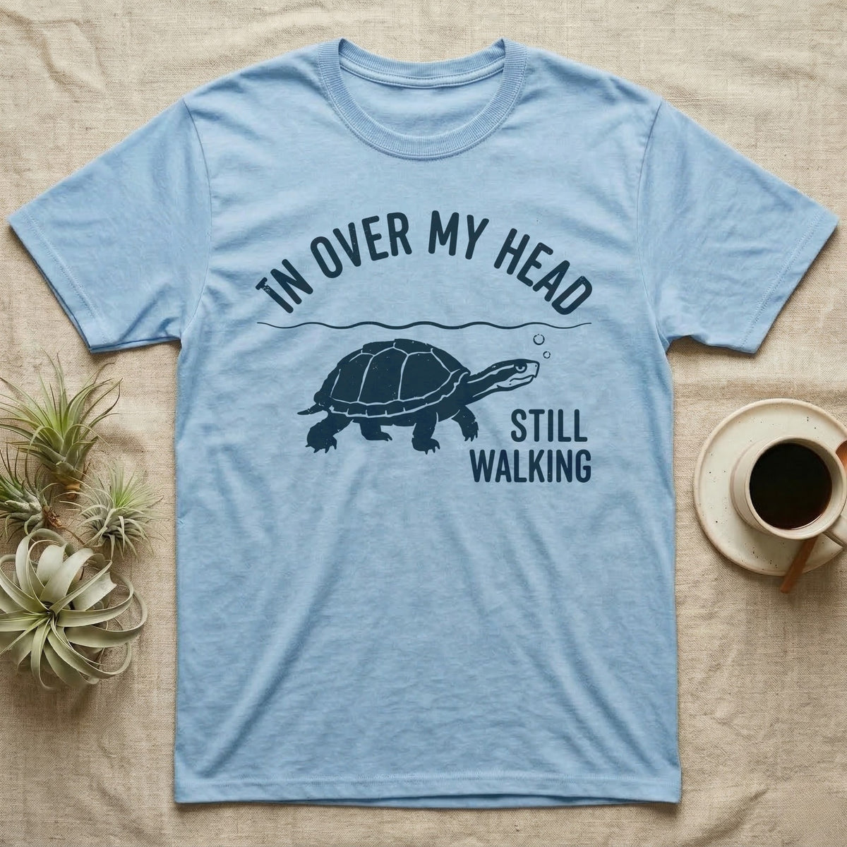 Musk Turtle Walking T-Shirt in Light Blue — Navy silhouette of a musk turtle walking under arched words In Over My Head, beside Still Walking