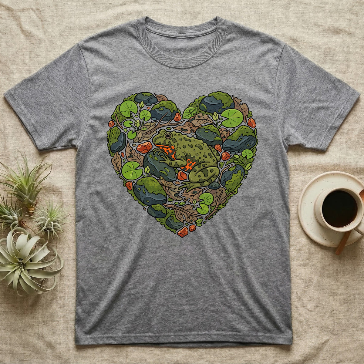 Grey t-shirt with a green frog and heart-shaped natural elements design.