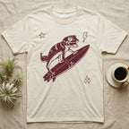 Knob-Tailed Gecko Surfing T-Shirt in Natural — Distressed one-ink illustration of a knob-tailed gecko riding a surfboard, airborne at the peak of an aerial.