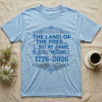 Corn Snake Still Missing Tee in Light Blue — Royal blue typographic tee reading The land of the free but my snake is still missing, with Victorian filigree and small coiled corn snakes.