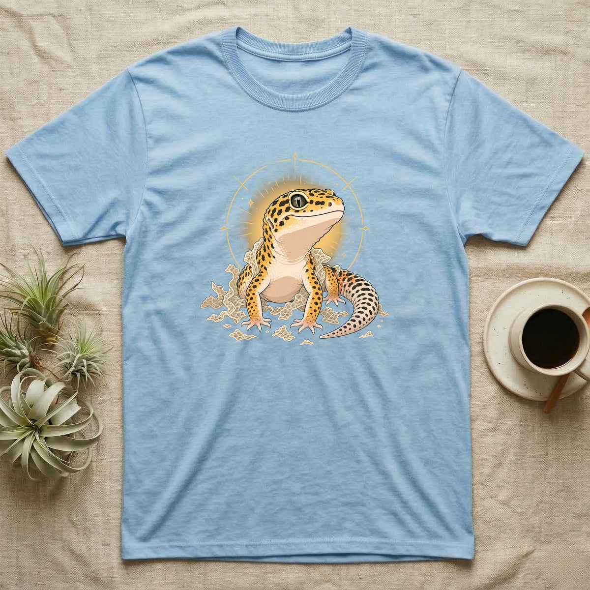 Leopard Gecko Shed T-Shirt in Light Blue — Bold vector illustration of a leopard gecko emerging fresh from a shed, lit by a soft warm halo glow.