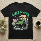 Green Basilisk Feral T-Shirt in Black — Green plumed basilisk sprinting across water below a dripping aqua-green metal "Walks On Water" wordmark