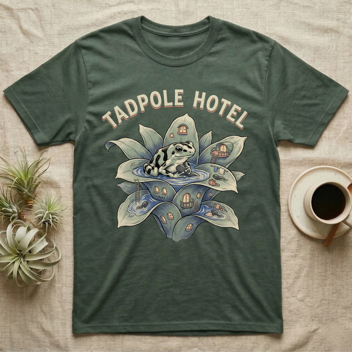 Tadpole Hotel Frog T-Shirt in Military Green — Whimsical naturalist illustration of a dart frog tucking tadpoles into a bromeliad Tadpole Hotel with hand-lettered marquee text.