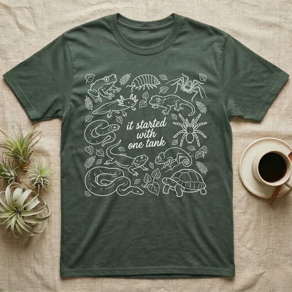 Terrarium Keeper One Tank T-Shirt in Military Green — White outline illustration of eleven terrarium species — bearded dragon, crested gecko, ball python, axolotl, tortoise, tarantula, isopod, whip spider, chameleon, tree frog and hognose — with pothos and fern leaves, ringed around the script line it started with one tank.