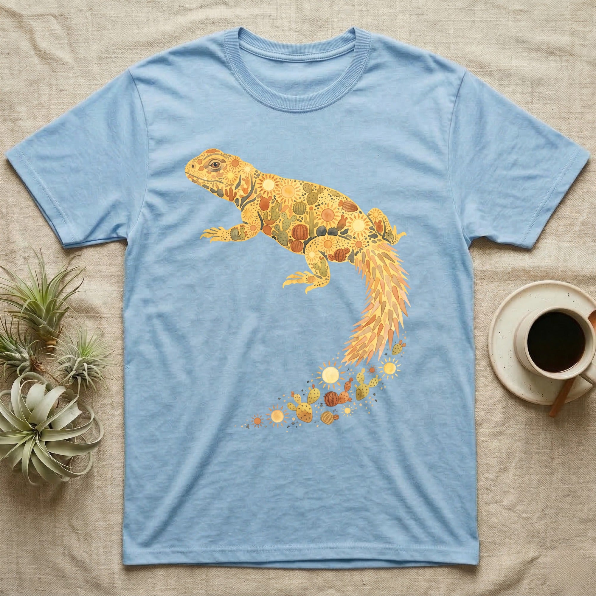 Uromastyx Solar Loaf T-Shirt in Light Blue — Warm watercolour mosaic of a basking uromastyx lizard made of tiny suns, cacti and sand on grey
