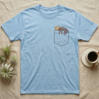 Hermit Crab Pocket T-Shirt in Light Blue — Cartoon purple pincher hermit crab peeking out of a chest pocket, its empty shell on the pocket edge