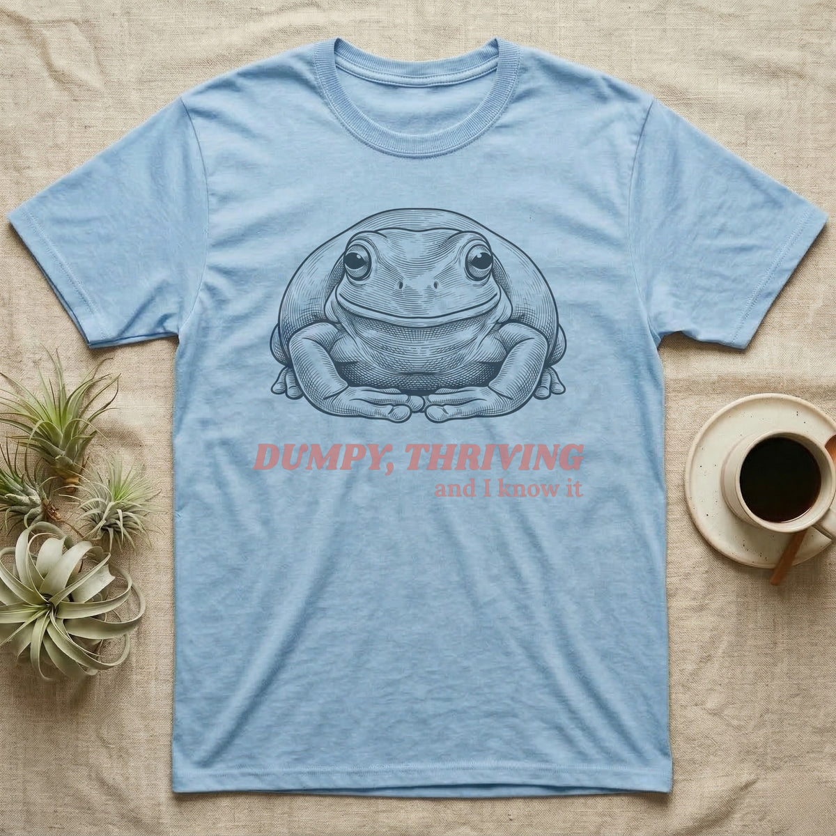 Dumpy Tree Frog T-Shirt in Light Blue — Engraved White's tree frog sitting square-on in a flat, tucked loaf pose under large retro lettering reading DUMPY, THRIVING, and I know it.