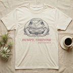 Dumpy Tree Frog T-Shirt in Natural — Engraved White's tree frog sitting square-on in a flat, tucked loaf pose under large retro lettering reading DUMPY, THRIVING, and I know it.