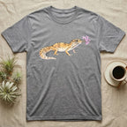 Leopard Gecko Blossom T-Shirt in Sport Grey — Watercolor illustration of a sandy-gold spotted leopard gecko holding a sand verbena blossom sprig, on a dark grey t-shirt.