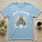 Asian Water Monitor Baby T-Shirt in Light Blue — Asian water monitor with tongue out among pastel reeds and lotus under puffy blue bubble text "just a puppy".