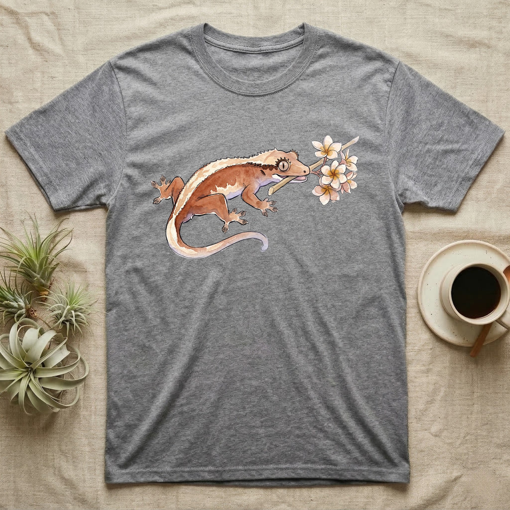 Crested Gecko Blossom T-Shirt in Sport Grey — Watercolor illustration of a rust-brown crested gecko holding a frangipani blossom sprig, on a dark grey t-shirt.