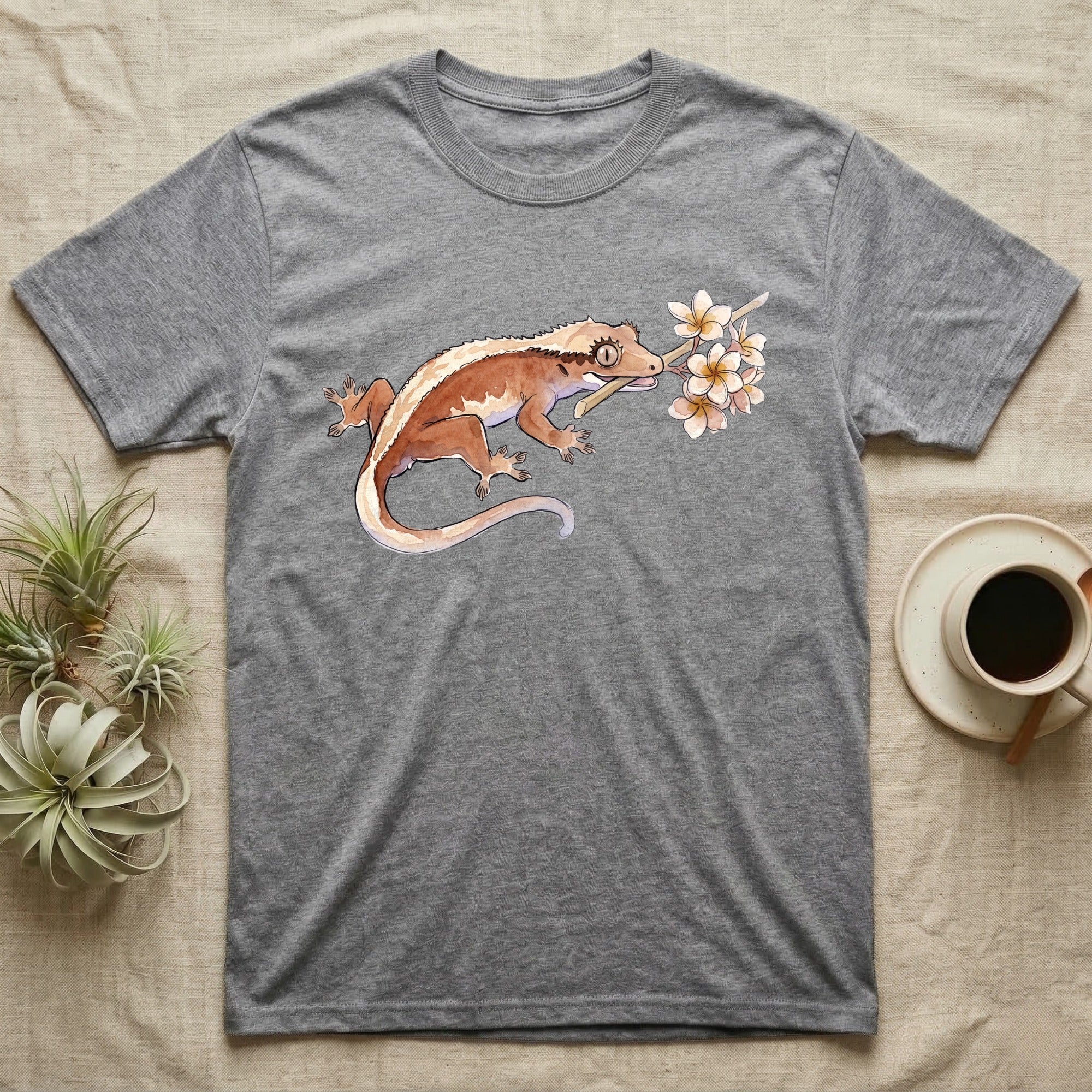 Crested Gecko Blossom T-Shirt in Sport Grey — Watercolor illustration of a rust-brown crested gecko holding a frangipani blossom sprig, on a dark grey t-shirt.