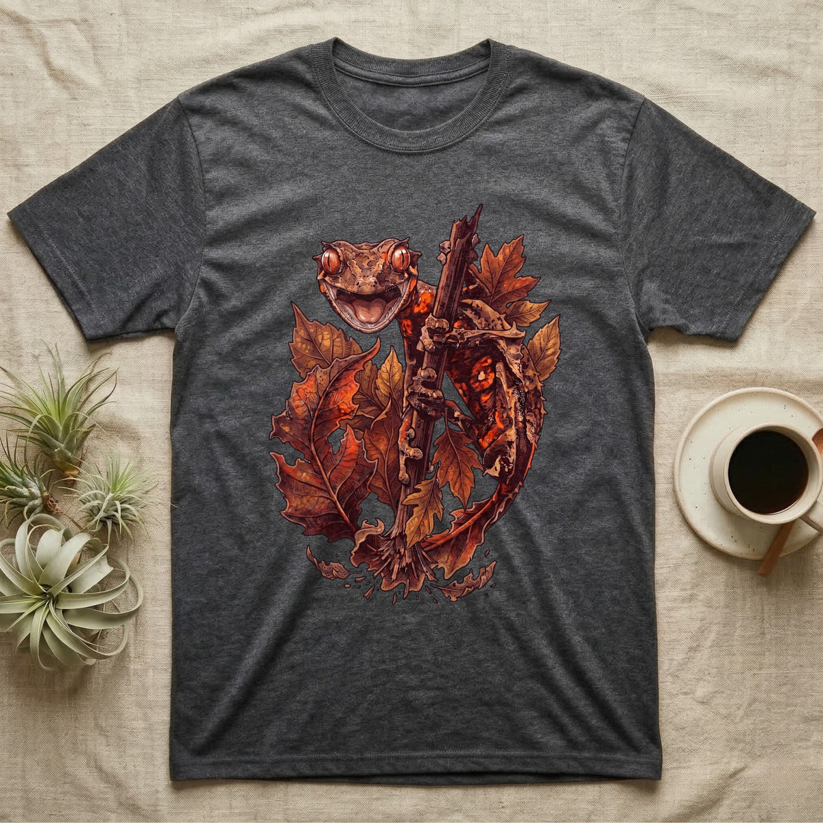 Satanic Leaf-Tailed Gecko Autumn T-Shirt in Dark Heather — Painted illustration of a satanic leaf-tailed gecko gripping a bare stem among dried autumn leaves in rust and amber, no on-shirt text.