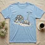 Tortoise Lawnmower Googly T-Shirt in Light Blue — Linocut illustration of a sulcata tortoise grazing beside a push mower wearing oversized googly eyes.