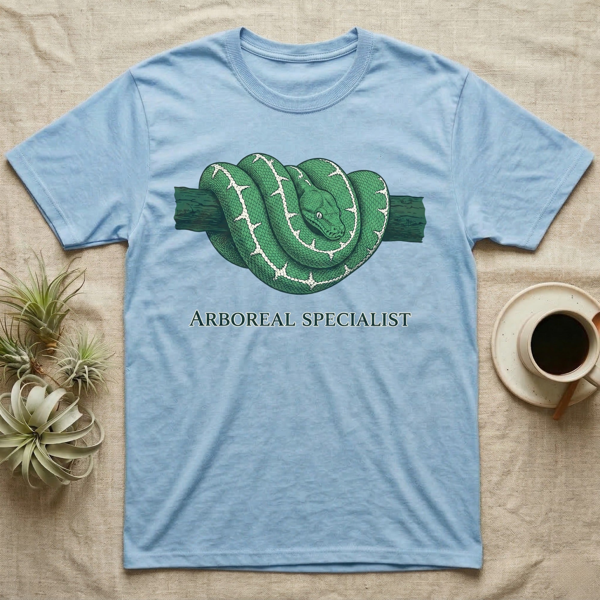 Light blue t-shirt with a green tree python coiled on a branch, text "ARBOREAL SPECIALIST".