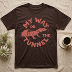 Ackie Monitor Tunnel T-Shirt in Dark Chocolate — Carved one-ink badge of an ackie monitor emerging from its sand tunnel, tongue out, ringed by the words MY WAY OR THE TUNNEL