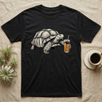 Slow Drip Tortoise T-Shirt in Black — Flat meme-style illustration of a sulcata tortoise reaching slowly toward a tall iced slow-drip coffee.