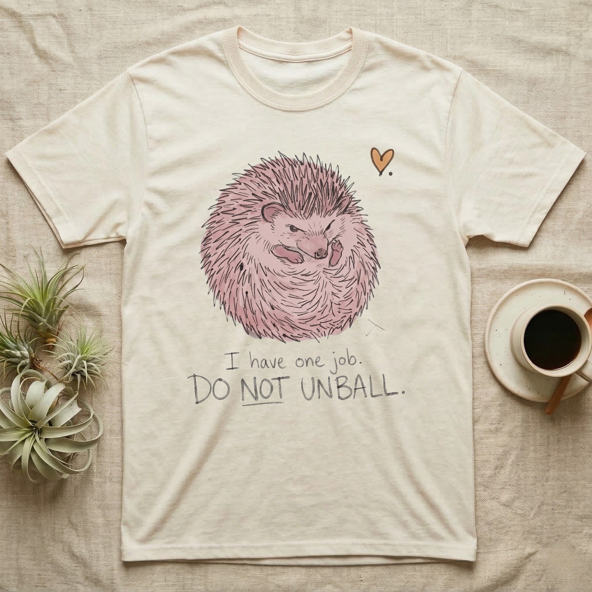 Hedgehog Do Not Unball Tee in Natural — Naive-doodle hand-drawn hedgehog curled in a tight defensive ball above a wobble-handwritten "Do Not Unball" label.